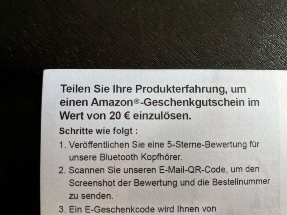 Ausschnitt einer Postkarte mit folgendem Text:

Teilen Sie Ihre Produkterfahrung, um einen Amazon®-Geschenkgutschein im Wert von 20 € einzulösen.

Schritte wie folgt:

1. Veröffentlichen Sie eine 5-Sterne-Bewertung für unsere Bluetooth Kopfhörer.

2. Scannen Sie unseren E-Mail-QR-Code, um den Screenshot der Bewertung und die Bestellnummer zu senden.

3. Ein E-Geschenkcode wird Ihnen von
