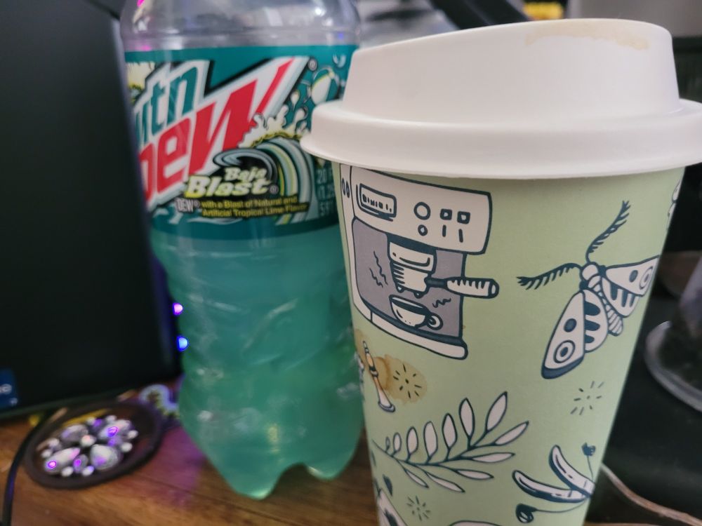 A close up of two drinks next to a computer tower. One is a partially drunk Mountain Dew Baja Blast, the other a generic large coffee cup with sketchy art on it. It is a large raspberry mocha. These will not be enough.