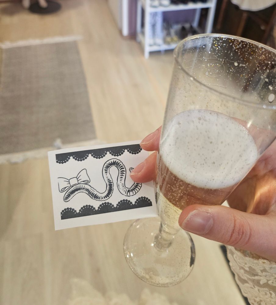 holding a glass of sparkling wine and a piece of paper with a worm wearing a headbow