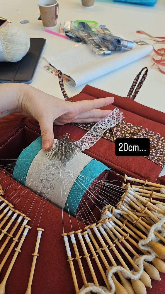 work in progress bobbin lace, with a hand and text indicating there's 20cm of lace made