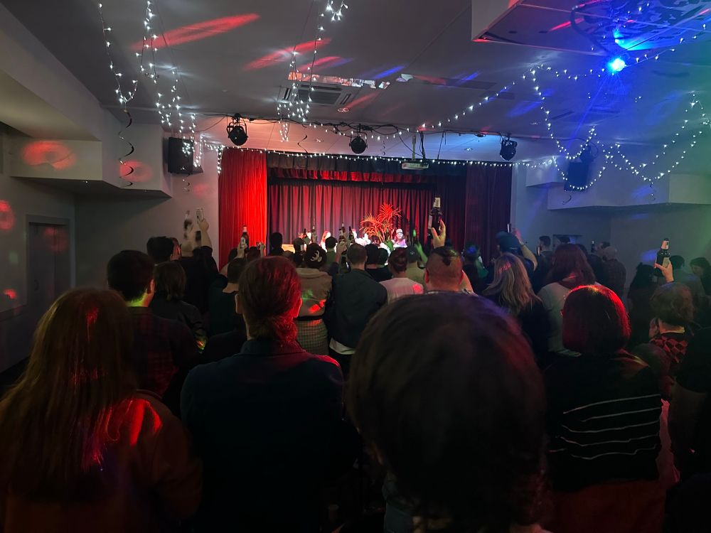 A photo taken from the audience of four podcasters sitting on a stage during a live show.