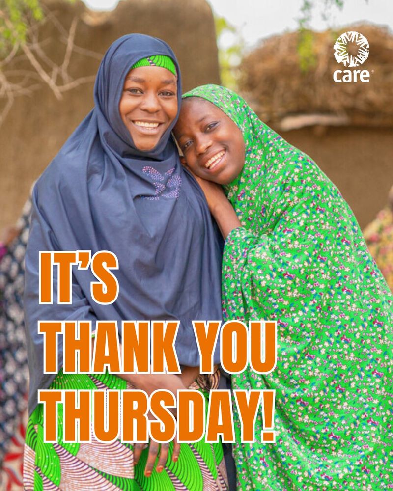 Two individuals smiling warmly and embracing each other, one dressed in a blue hijab and the other in a green patterned hijab, in front of a textured clay wall. Text overlay says "IT'S THANK YOU THURSDAY!" with the CARE organization logo at the top.