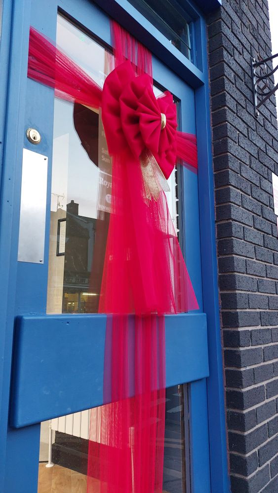 Red ribbon decoration on blue door with glass windows reflecting the street