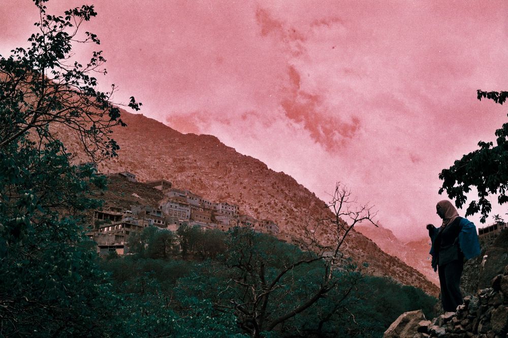 Un paysage en lomochrome, on voit une femme à droite et une ville au fond. Le ciel est rose et le sol vert bleuté.