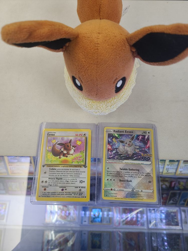An eevee plush looking down at a couple eevee Pokémon cards
