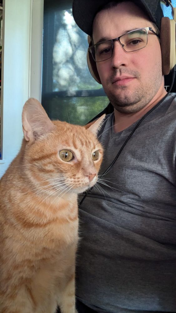 Chuck sits at his desk with headphones on. Fat Betty, the orange cat, stares intensely out of a window that is out of frame from his lap.