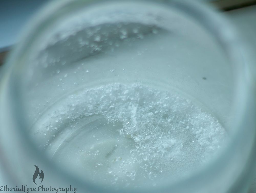 A near empty glass jar of bath salts, viewed through the open rim. 