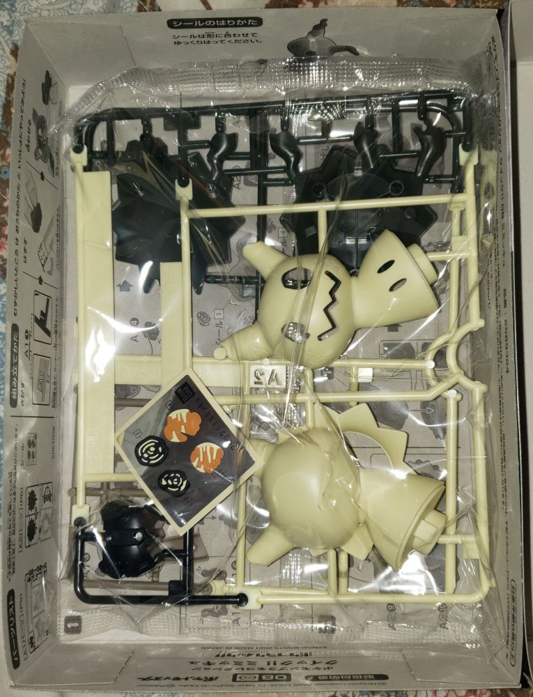 A look inside the cardboard model kit box. There are images and instructions printed directly into the insides of the box, including the walls, all in black ink, depicting how to put the model together. The model itself is in a rectangular plastic factory sealed bag, not unlike a bag of chips. Inside the bag are two or more plastic-wire "gunpla" style assemblies containing the parts and pieces of the model kit; most are cream colored but some are black. These parts can be snapped off, but I plan on cutting them out with my specific model kit cutting pliers. Painting the model isn't required. There is also a small square sheet with stickers for the Pokemon's Pikachu disguise: the swirly scratchy drawn-on black eyes and red cheeks.
I love Mimikyu, don't you? It just wants to be appreciated and loved too. It feels very left out and unnoticed. Other Pokemon like Pikachu get all the attention and love. Everyone wants to be loved and appreciated. Is that so wrong? Poor Mimikyu...