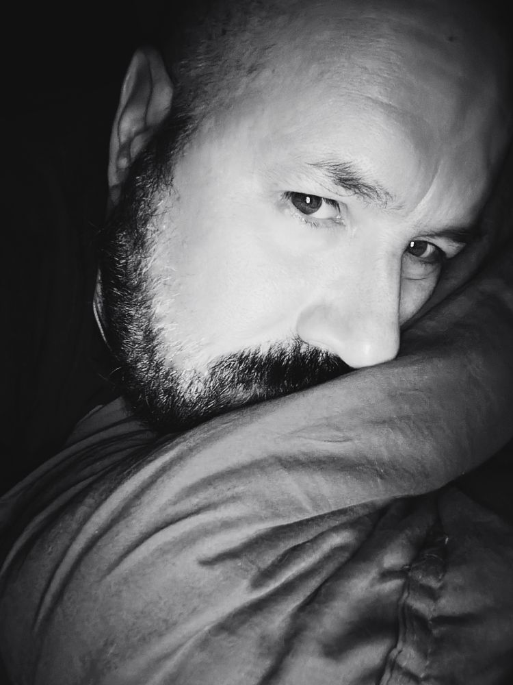 Black and white selfie. I'm a bear man with mustache and beard laying despondently in bed.