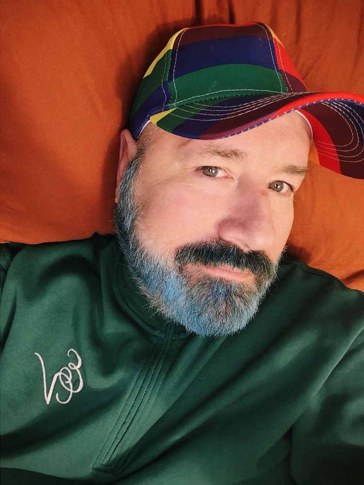 Selfie. I'm a bear man with blue mustache and beard wearing a green shirt and rainbow cap.
