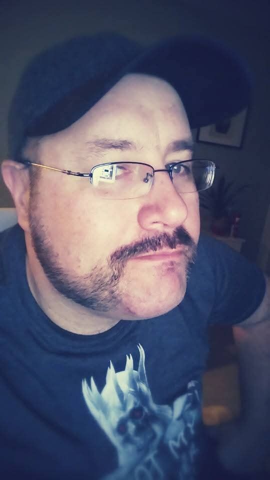 Selfie. I'm about 40 years old, wearing a black cap, thin eyeglasses, and a black shirt with a Dark Souls graphic on it. I have a mustache and beard, but the goatee area is shaved clean.