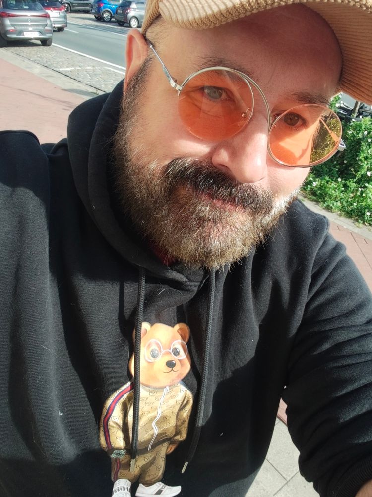 Selfie. I'm a bear man with mustache and beard wearing a black hoodie with a cartoon bear on it, and amber-tinted eyeglasses.