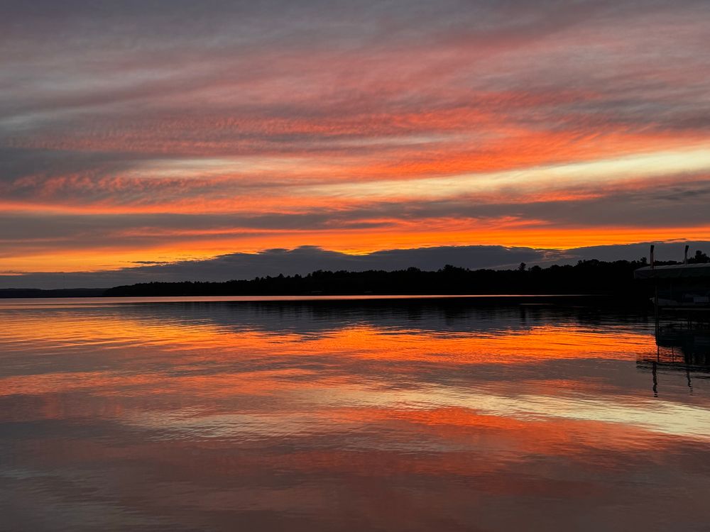 An orange sunset is reflected off the surface of a calm lake.