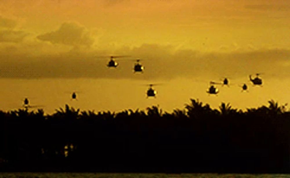 a group of helicopters flying over a body of water at sunset