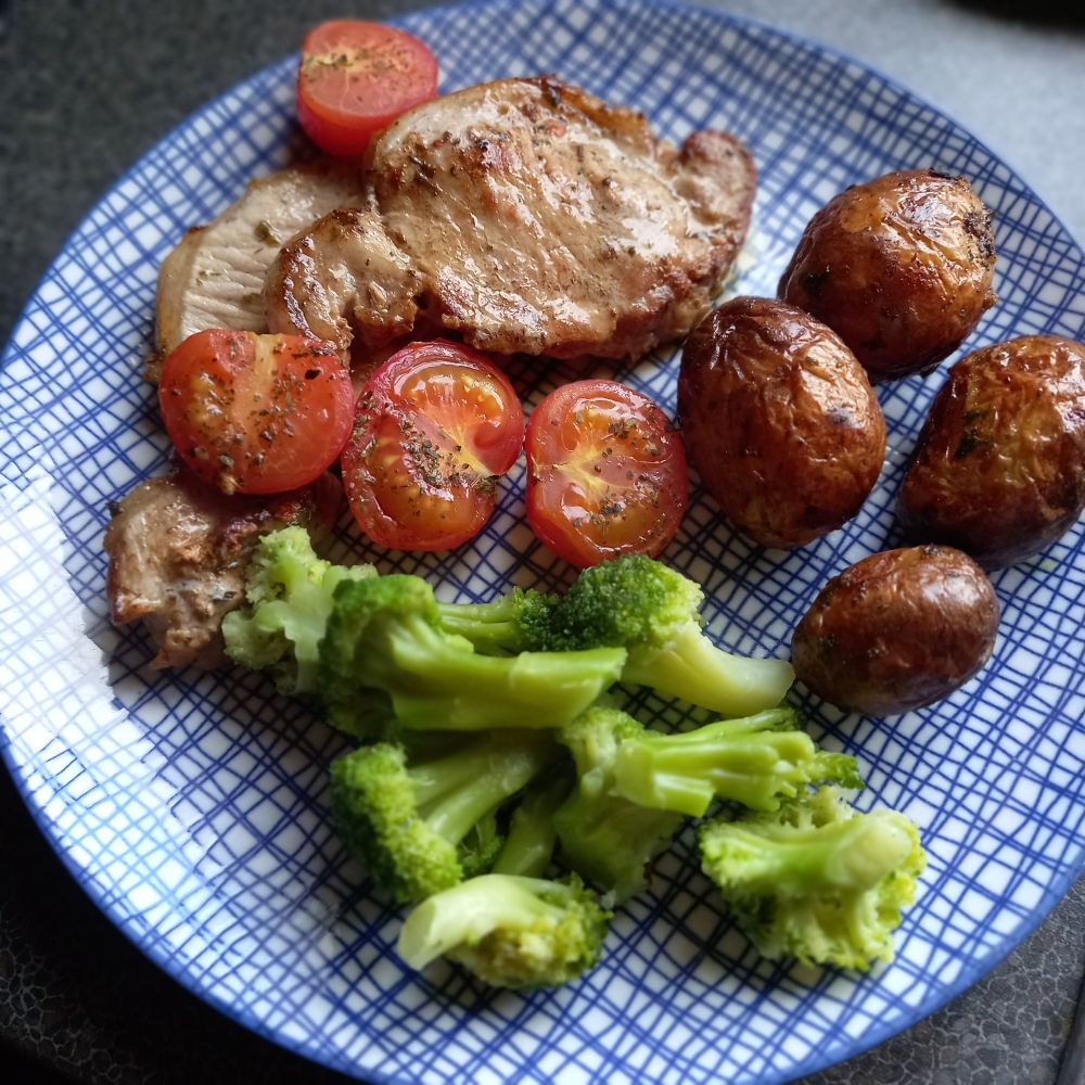 Blue plate with panfried pork chops, roast tomatoes, potatoes and broccoli.