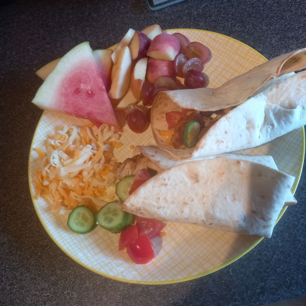 A plate with two filled wraps, various fruits, salad bits and cheese. The 12 year old will devour this!