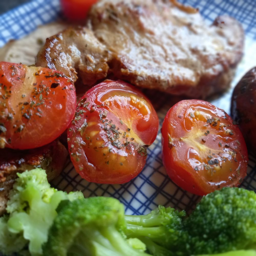 Close up of tomatoes and pork chops on a blue plate. They look juicy and are seasoned with basil! 