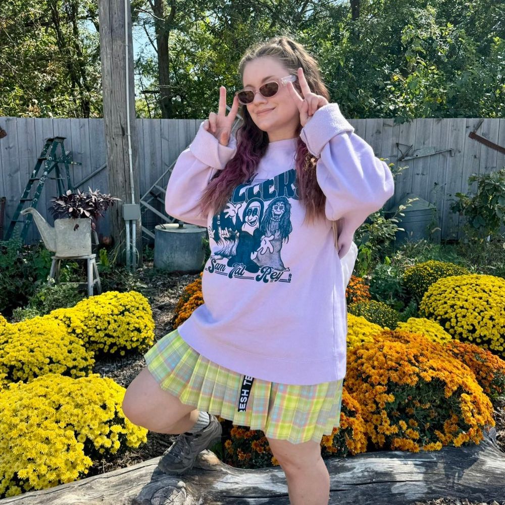 The Lady Killers crewneck being rocked in front of a fall-colored flower bed