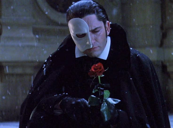 phantom of the opera guy holding a rose sadly while in the snow 