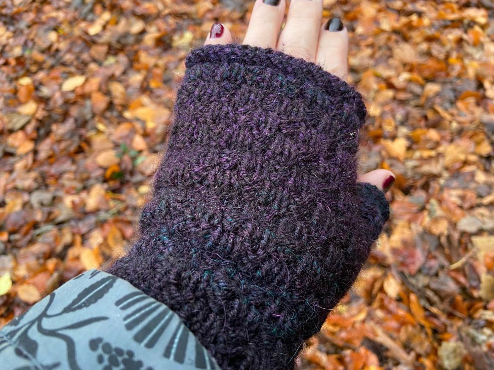 One hand wearing a textured knitted fingerless mitten.