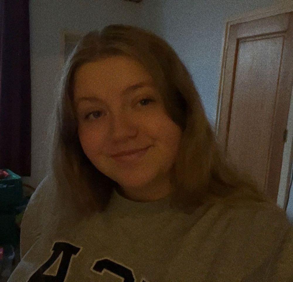 A selfie of me in my living room wearing a grey sweater and smiling, I also have my hair down