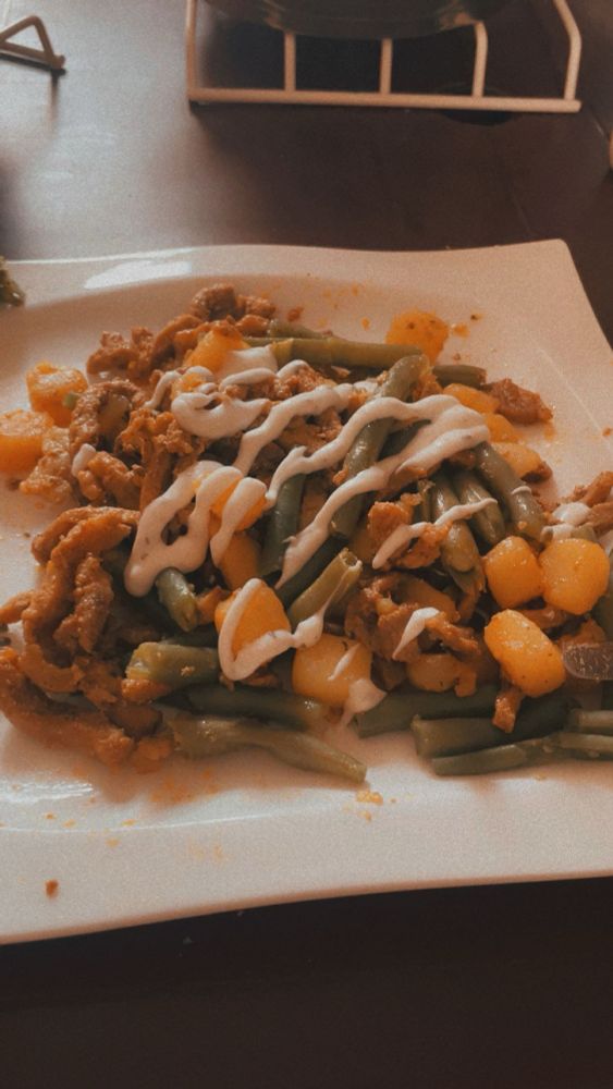 A plate of food, specifically shawarma, green beans, potatoes and garlic sauce 