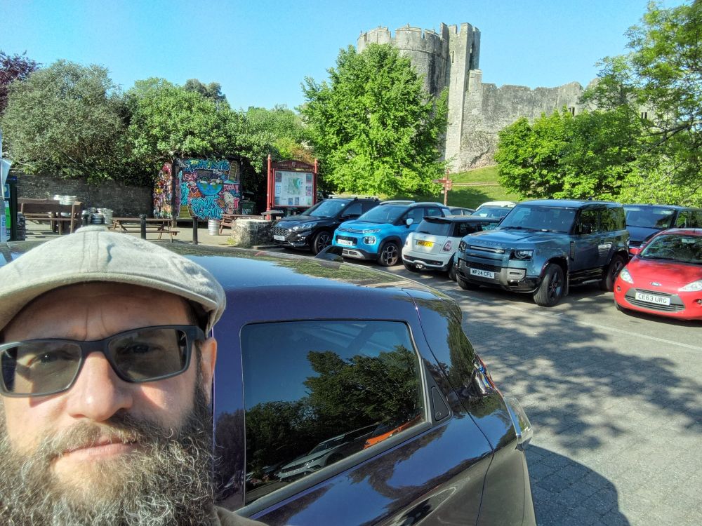 Me smiling in the sunshine, in a car park with a castle in the background