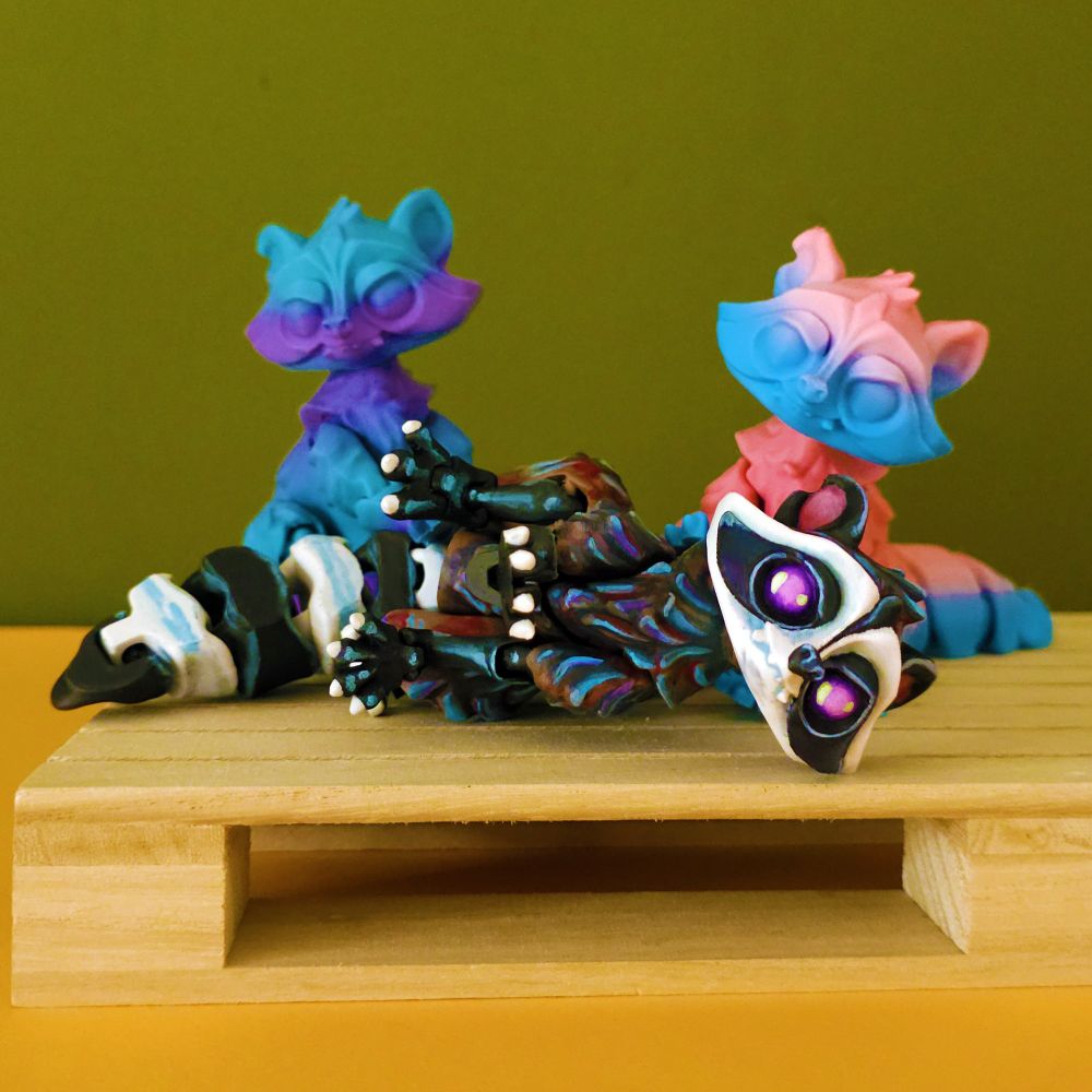 3d printed and handpainted raccoons sitting on a wooden platform, on a green background, there is three of them now, oh no
