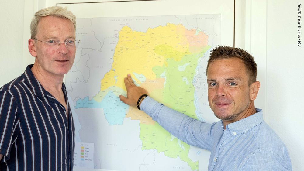 Prof. Dr. Axel Fanego Palat (links) von der Goethe-Universität Frankfurt und Prof. Dr. Nico Nassenstein (rechts) von der JGU vor einer Landkarte, die den afrikanischen Kontinent zeigt (Foto/©: Peter Thomas / JGU)