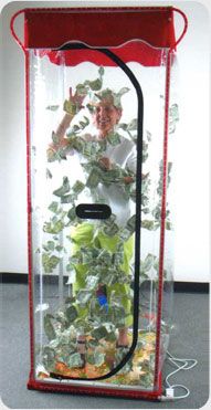 A person standing in one of those money air machines trying to grab the money.