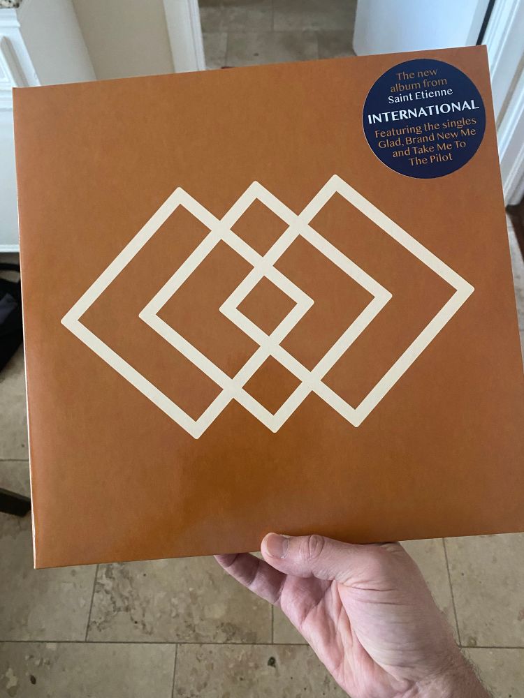 The cover to Saint Etienne’s 2025 album “International.” A dark orange cover with three interlocking diamond shapes in white.