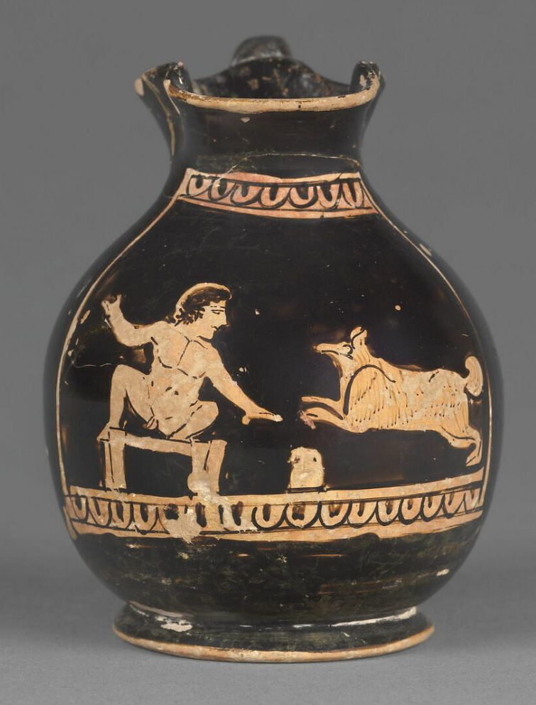 Oenochoé miniature fabriquée à Athènes à la fin du Ve siècle avec notre ère mettant en scène un chien courant vers un petit garçon juché sur une table, un oenochoé est disposé à côté rappelant le contexte dionysiaque de la scène.
Conservé au musée du Louvre, CA 2910