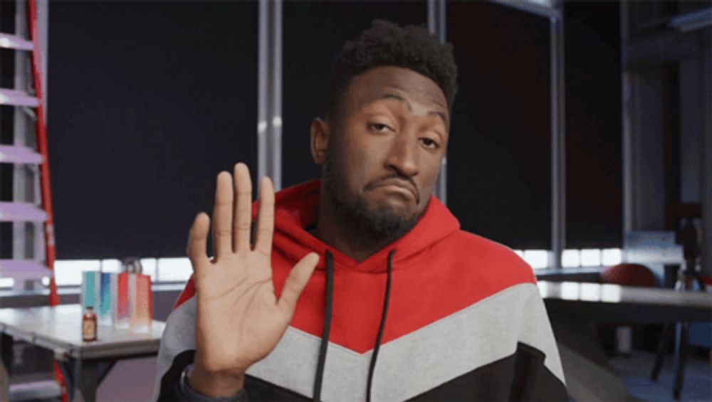 a man wearing a red white and black hoodie holds up his hand