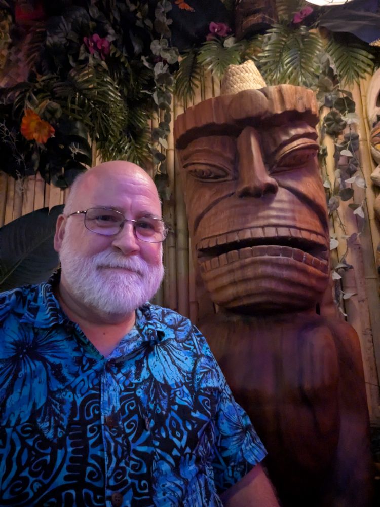 GupDaddy next to a carved wooden tiki with a straw hat perched atop its head.
