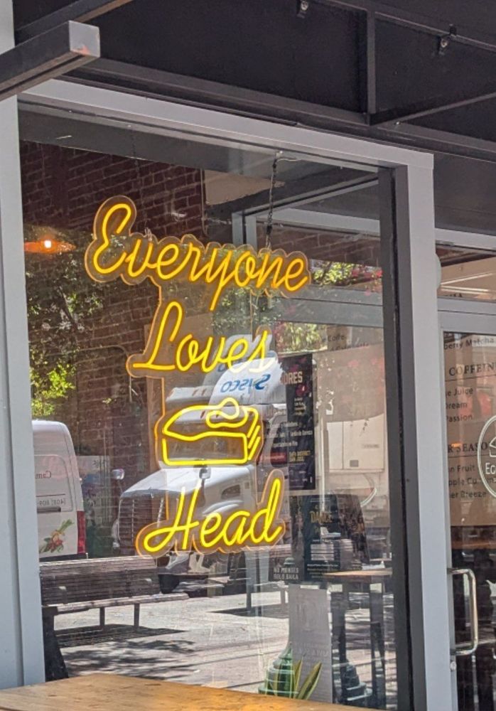 A neon sign in a window that reads "Everyone Loves Head"