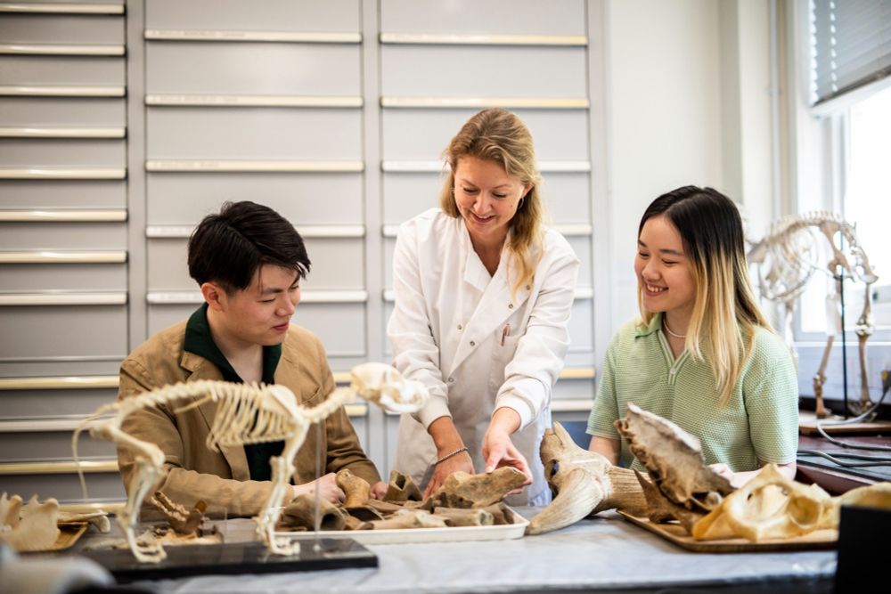 A female researcher wearing a lab coat guiding students.
