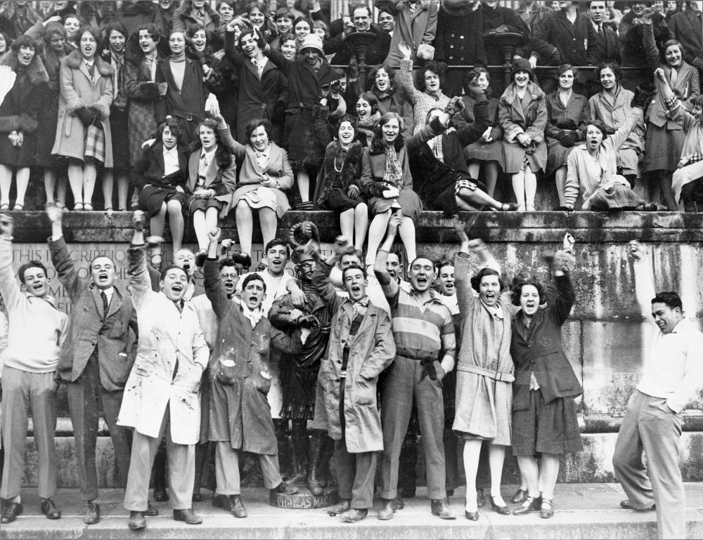 A black and white photo of a group of people smiling and raising their hands.