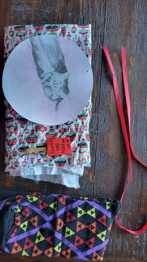 Opened presents! Fabric Xmas wrap, folded, and the beautiful hand-drawn cat label and a radical pin badge on top.badge says "It's not the 1950s you c*nts". Also, pressing 2, a pair of snug socks with triangle coloured pattern on black
