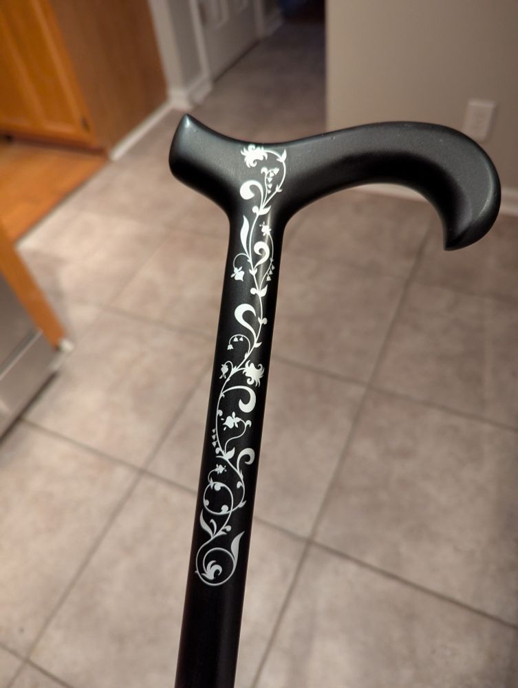 The top third of a black cane with silver embellishment on the side in the pattern of lillies of the valley