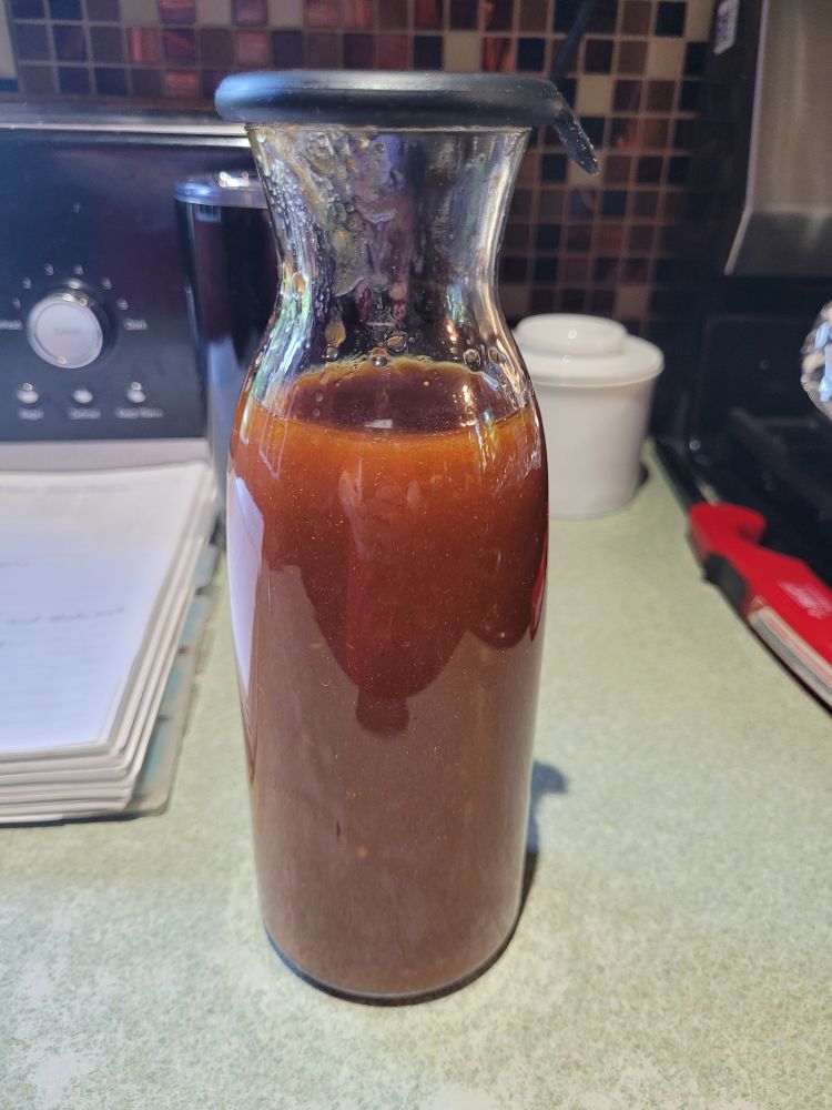 A glass carafe with a silicone cap, filled with homemade red French salad dressing. 