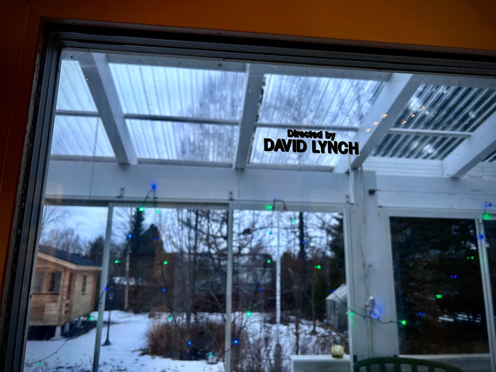 A window text sticker in house’s window. Text reads Directed by David Lynch.
