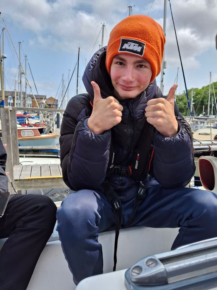 A young person sat on deck with his thumbs up
