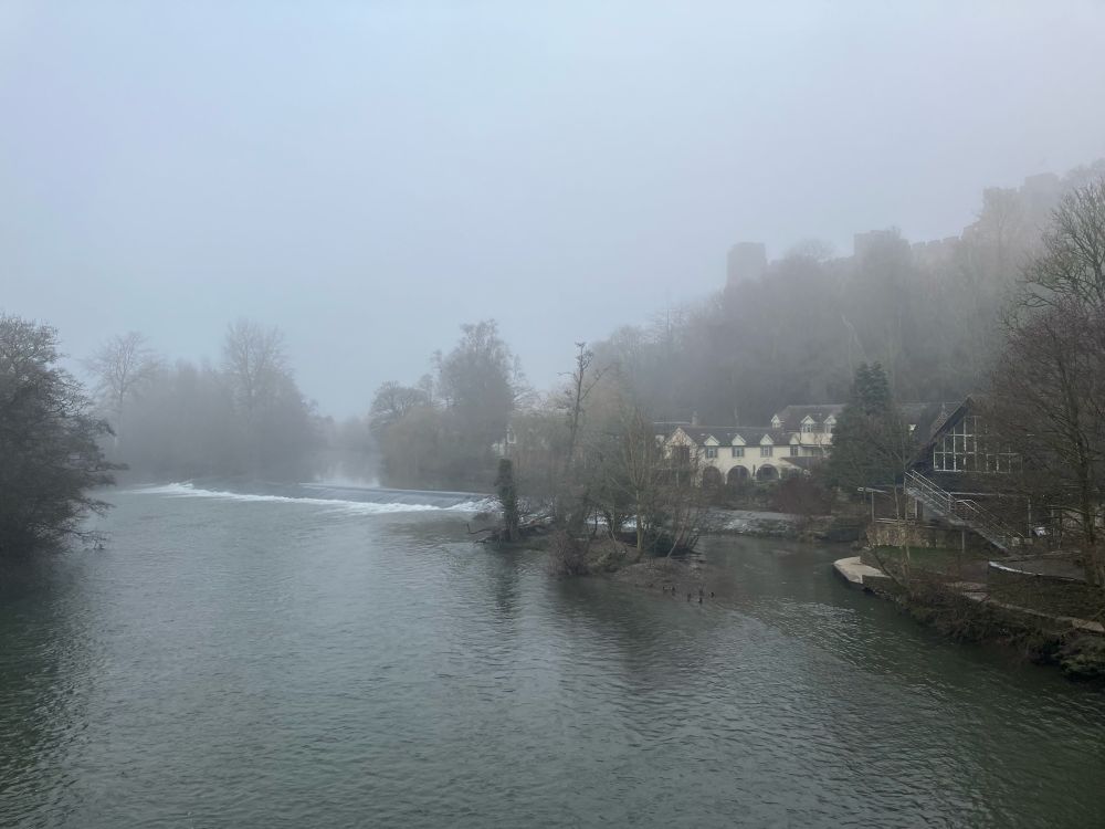 Looking north from Dinham Bridge in Ludlow, a misty view of the River Teme and Dinham Weir with the castle above enshrouded in mist.