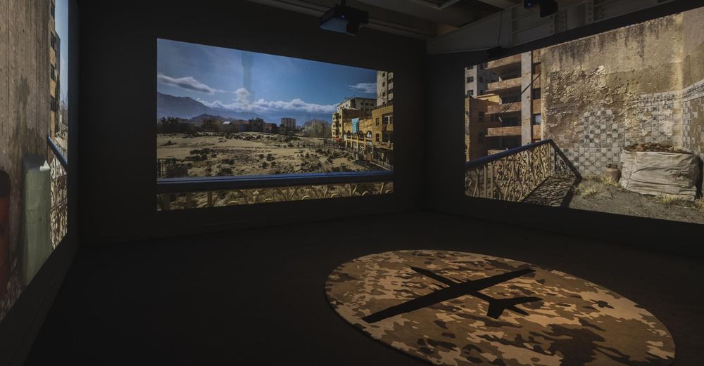 A photograph of the installation - three screens on three walls depict different views of the same scene, rendered in Unreal Engine, of a town