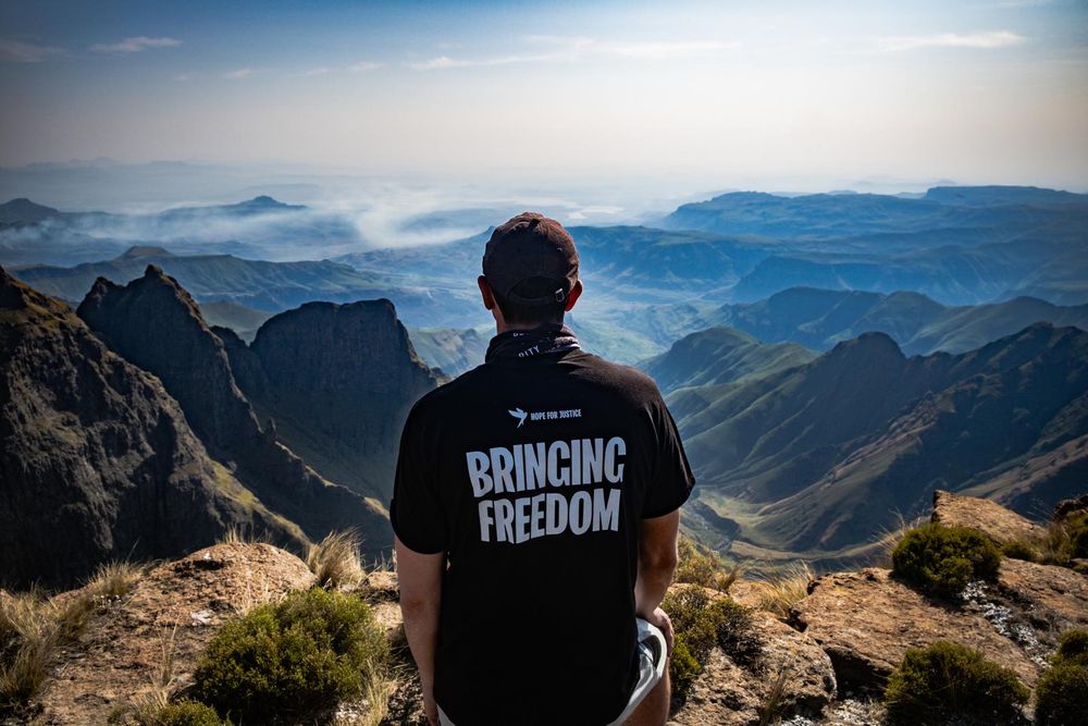 Hope for Justice CEO Tim Nelson looks out over the Drakensberg mountains, wearing a tshirt reading BRINGING FREEDOM