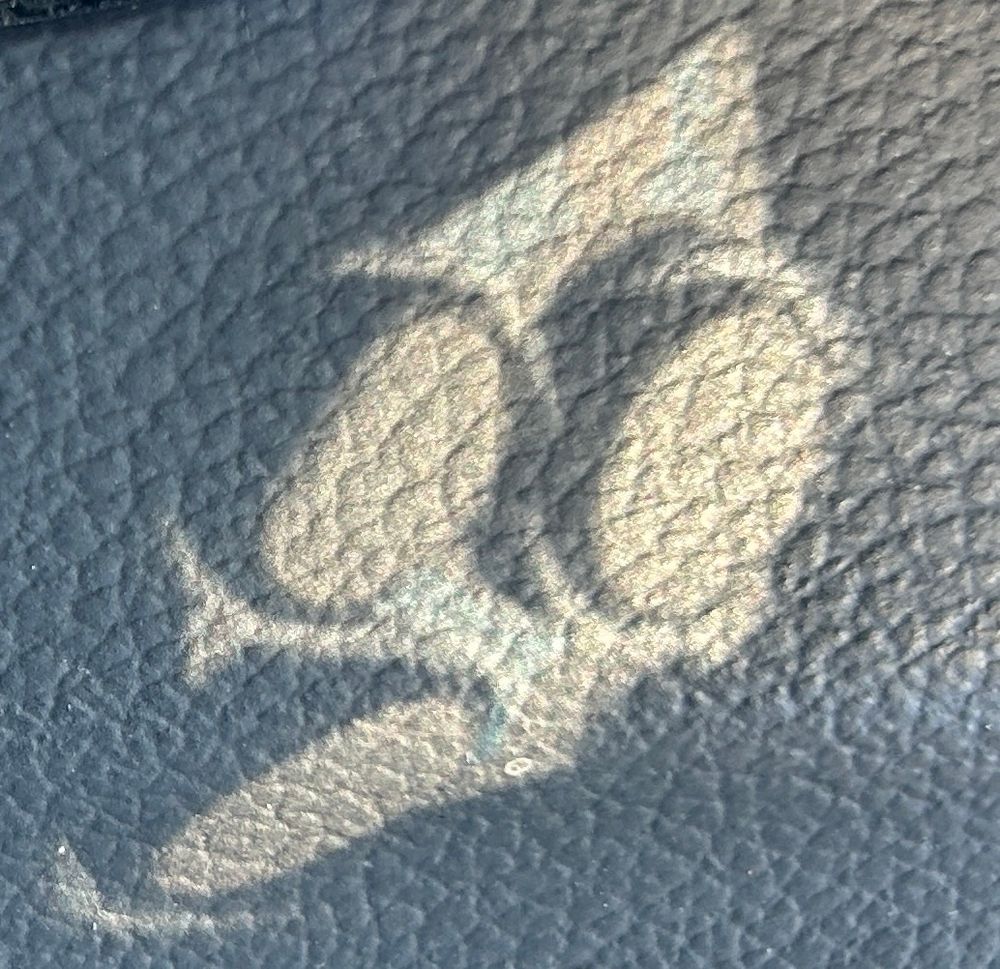 Shadow of the three-ring camera lenses of the iPhone on the textured surface of a steering wheel. It looks a little like a face expressing surprise 