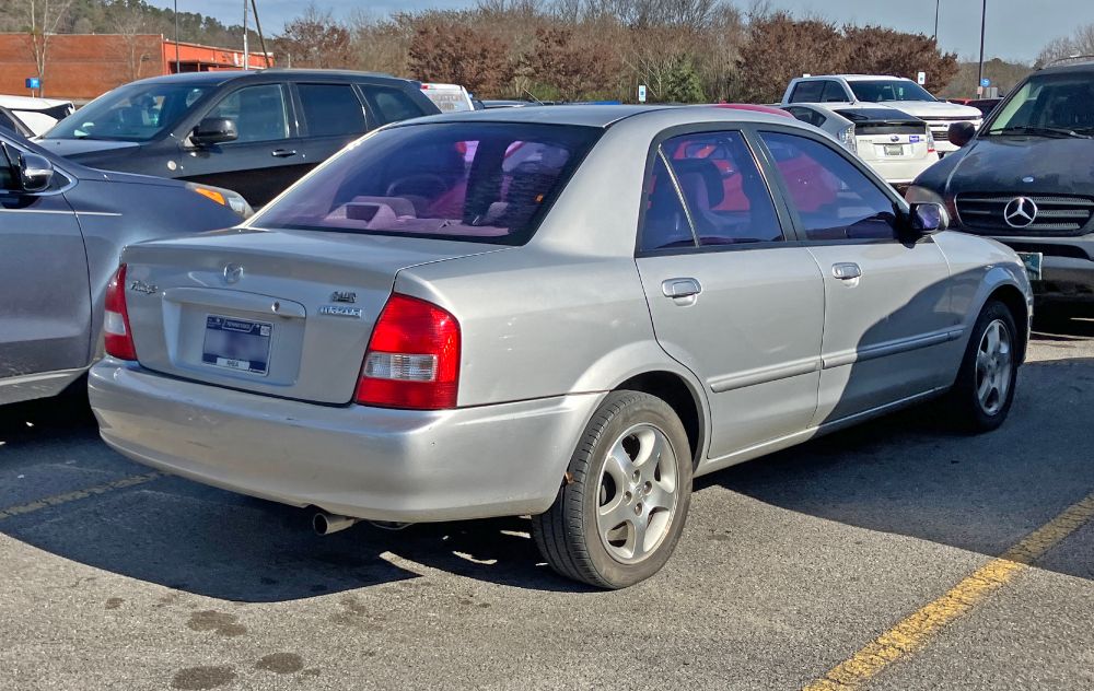 Right rear view of a silver 9th generation Mazda Protegé in a Walmart parking lot.