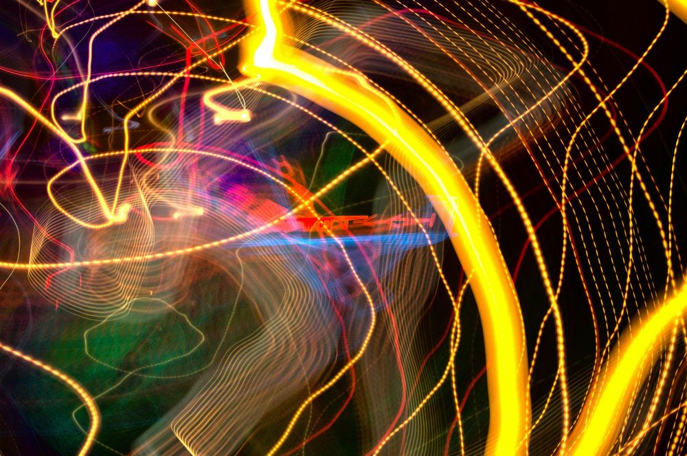 Auto-generated description: Vibrant light trails intertwine in an abstract pattern of swirling colors, including yellow, red, and blue.