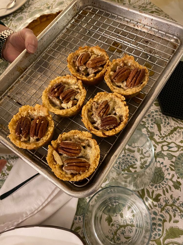 Pecan pies (each the size of a muffin) paced on a tray. The pies are each topped with two pecan halves