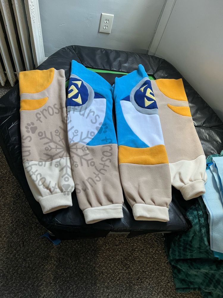 Sleeves and legs of a kigurumi laid out. They are tan with orange markings, and ivory ends. The legs have blue protogen armor on the upper halves, with yellow markings shown better in the next photo.